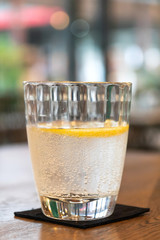 Glass of sparkling water with lemon slices on wooden brown table with blur bokeh background.