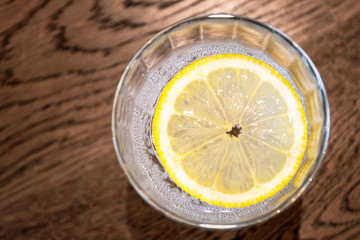 Glass of sparkling water with lemon slices on wooden brown table. Top view