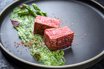 Blanched green asparagus tips with barbecue dry aged wagyu fillet steak and avocado coriander relish as top view on a modern design plate
