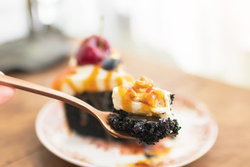 Small bite of dark beer chocolate cake on fork (Chocolate Stout Cake) with caramel sauce and walnut on top; the remainder of the cake in the background.