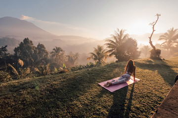 woman with dark hair in sportive suit making yoga on sunrise with volcano Agung view