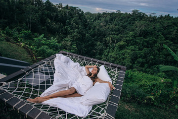 beautiful woman with dark hair relaxing in open air  bed with Bali jungle view