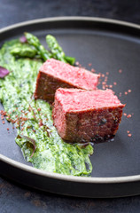 Blanched green asparagus tips with barbecue dry aged wagyu fillet steak and avocado coriander relish as closeup on a modern design plate