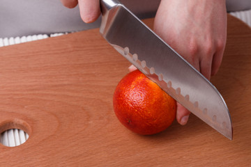 young woman in a gray apron cuts blood orange