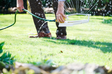 Obraz na płótnie Canvas Man living water sprayer using nozzles to hydrate the garden grass during hot dry summer season