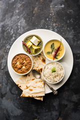 Indian vegetarian  platter / Thali having Palak paneer butter masala, dal makhani, flat bread or naan and rice served in a white plate