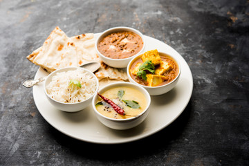 Indian vegetarian  platter / Thali having Palak paneer butter masala, dal makhani, flat bread or naan and rice served in a white plate
