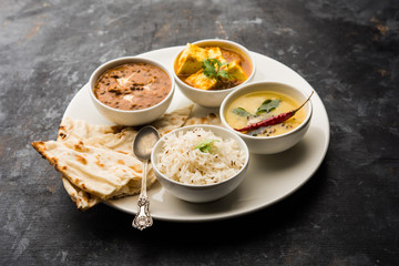 Indian vegetarian  platter / Thali having Palak paneer butter masala, dal makhani, flat bread or naan and rice served in a white plate