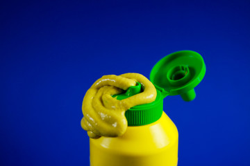 Close up of paste of mustard squeezed out a plastic bottle with blue background