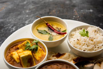 Indian vegetarian  platter / Thali having Palak paneer butter masala, dal makhani, flat bread or naan and rice served in a white plate