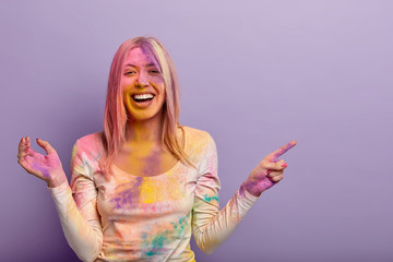 Overjoyed European woman laughs from positive impressions, shows place where Holi festival is held,...