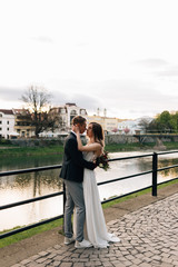 the bride and groom happy and funny on their wedding day are walking along the embankment by the river