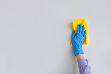Employee hand in blue rubber protective glove wiping wall from dust with dry rag. General or...