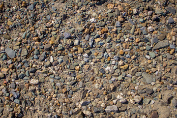 gray white blue yellow stones of different sizes and shapes on the light sand. rough natural surface texture