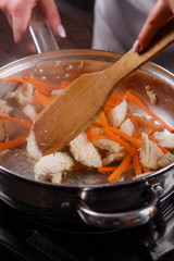 young woman in a gray aprons roasts chicken fillet with carrots
