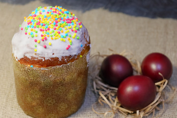 Easter cake in white glaze and sprinkling of colored sweet balls. Painted Easter eggs.