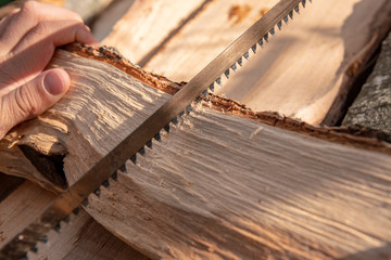 Hand holds a firewood and saws it into the corresponding pieces with a fretsaw.