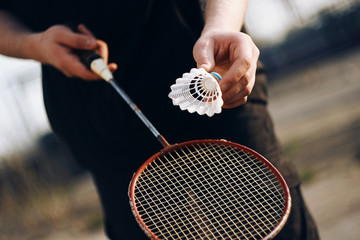 A human in black clothes holding a racket and is going to throw a shuttlecock. A pleasant outdoor activity is playing badminton on a Sunny day.