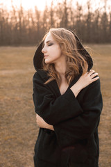 Portrait of the young woman in black cape on the field. Profile