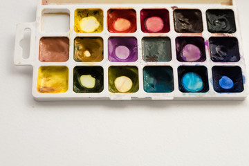 Bright colorful watercolor paints with palette on a white background. Close-up watercolor tray. Flat lay, top view, copy space. School and creativity concept