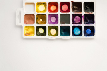 Bright colorful watercolor paints with palette on a white background. Close-up watercolor tray. Flat lay, top view, copy space. School and creativity concept