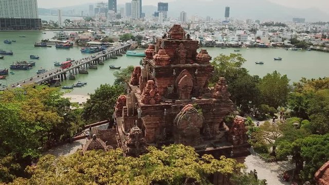 Aerial forward cityscape Po Nagar Cham temple tower Vietnam Nha Trang. Modern buildings city bridge active road traffic cars river fishing old boats. Authentic culture style Asia. Sunny day. Landmark