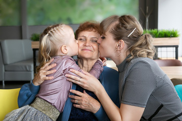 Daughter and granddaughter hug and kiss grandmother. A little girl and a young woman hug their...