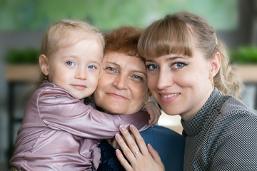 Fototapeta premium Daughter and granddaughter hug and kiss grandmother. A little girl and young woman hug their elderly mom and grandmother tightly.