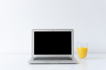 Open laptop and glass of orange juice on the desk with white background