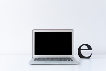 Open laptop and wooden black initial letter on the desk with white background