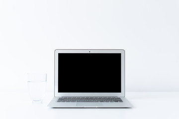 Open laptop and glass of water on the desk with white background