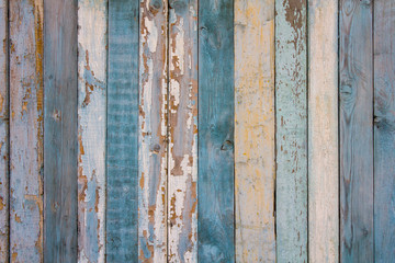 old yellow blue white wooden wall fence of wooden boards with peeling paint. vertical lines. rough surface texture