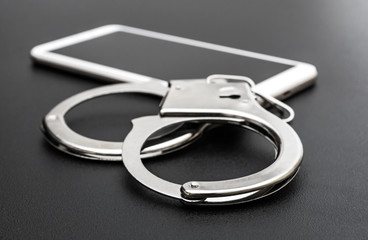 Smartphone with handcuffs on black background.