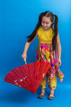 Adorable Asian little girl with long black hair in pig tails and sleeveless summer dress standing twirling a painted red silk umbrella
