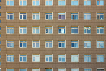 the gray facade of a high-rise multi-storey office building with white blue square windows