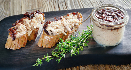 meat rillettes with vegetable jam on black serving board with fresh thyme and a glass jar with the jam covering rillettes 