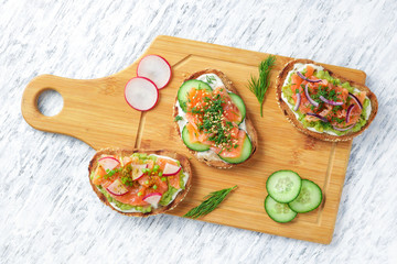 healthy sandwiches with rye bread salmon cream cheese avocado cucumber dill red onion radish on cutting board top view