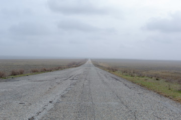 Wide old road in the foggy steppe