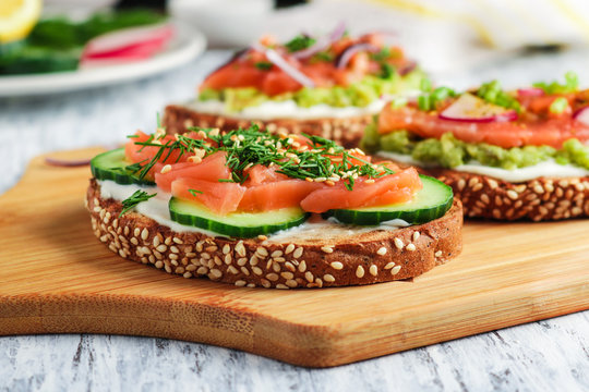 Open Sandwiches With Toast Bread Smoked Salmon Cream Cheese Sliced Cucumber Dill Avocado On Wooden Cutting Board Close Up Selective Focus