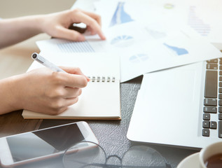 Business concept. Woman takes note for project with laptop and report in office desk. Backlighting, sun glare effect, close up, side view, copy space