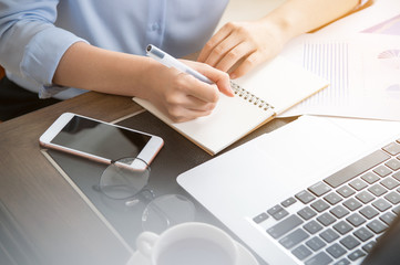 Business concept. Woman takes note for project with laptop and report in office desk. Backlighting,...