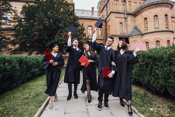 young graduated students making team gesture with rolled diplomas1