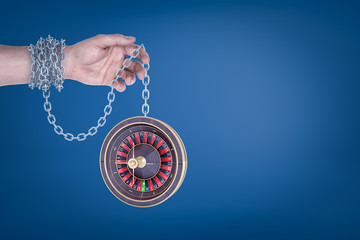Male hand chained to a roulette on blue background
