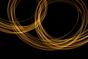 Long exposure, light painting photography.  Vibrant loops of metallic gold colour against a black background