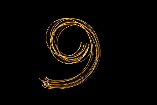 Long exposure, light painting photography.  Single number in a vibrant neon metallic yellow gold colour against a black background