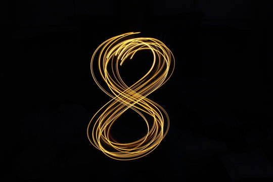 Long exposure, light painting photography.  Single number in a vibrant neon metallic yellow gold colour against a black background