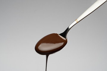 Liquid chocolate on a spoon on light grey backgiund