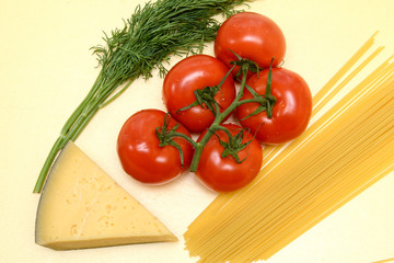 On a yellow background, red tomatoes on a green branch, a slice of yellow cheese, spaghetti pasta, dill twigs. Concept - healthy food. Top view