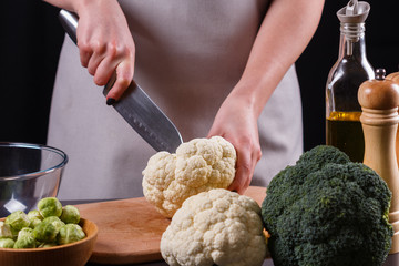 young woman in a gray aprons cuts cauliflower broccoli