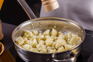 young woman in a gray apron roasts cauliflower broccoli